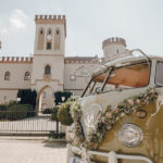 Hochzeitsauto mit Blumenschmuck vor Schloss.